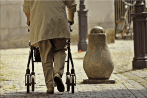 Image of an older person using a walker to go down a sidewalk.