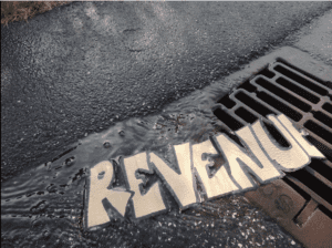 Image of the word "Revenue" written on paper going down a street drain.
