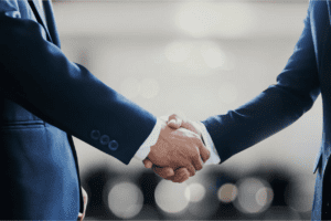 Two male wearing blue suits, they are doing a handshake.