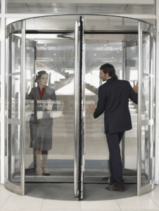 A white man and a white woman are shown looking at each other as they go through a revolving door.